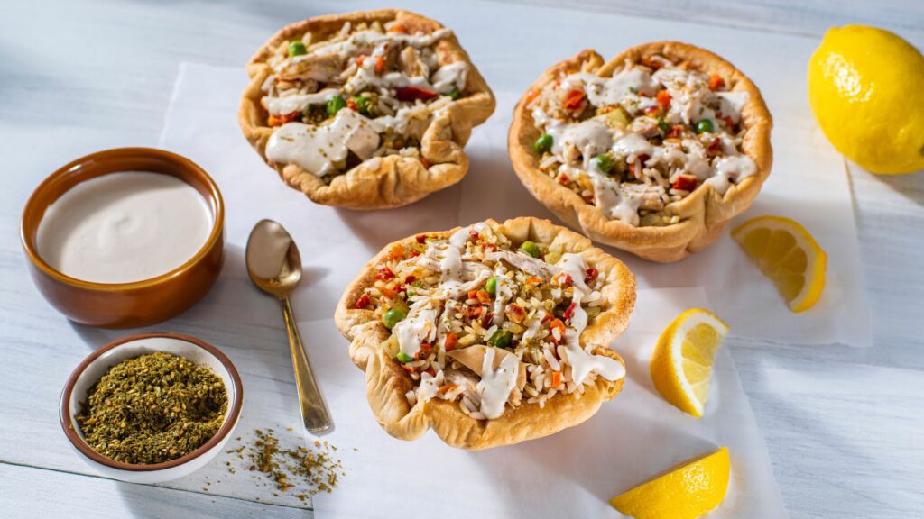 baked pita bowls stuffed with mediterranean style chicken rice peas carrots bell peppers and tahini sauce